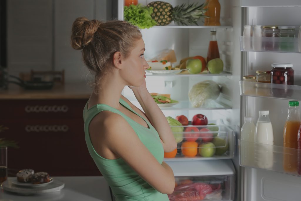 Lány áll a nyitott hűtőszekrény előtt és nem tudja mit főzzön