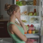 Lány áll a nyitott hűtőszekrény előtt és nem tudja mit főzzön