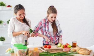 Két fiatal nő a konyhában zöldséget vág