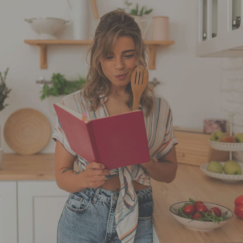 Fiatal nő a konyhában szakácskönyvet olvas